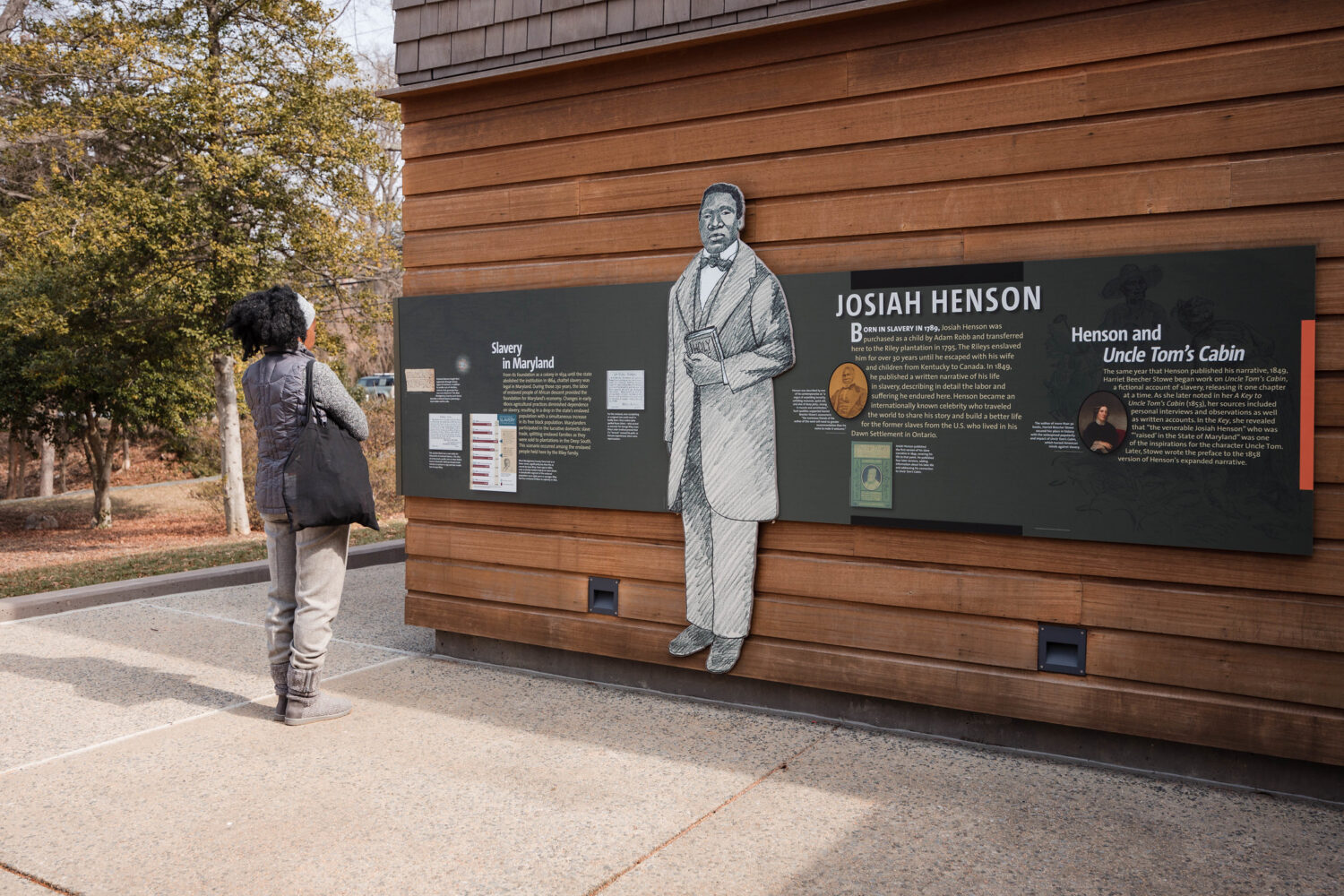 An adult reads a display outside of Josiah Henson Museum and Park