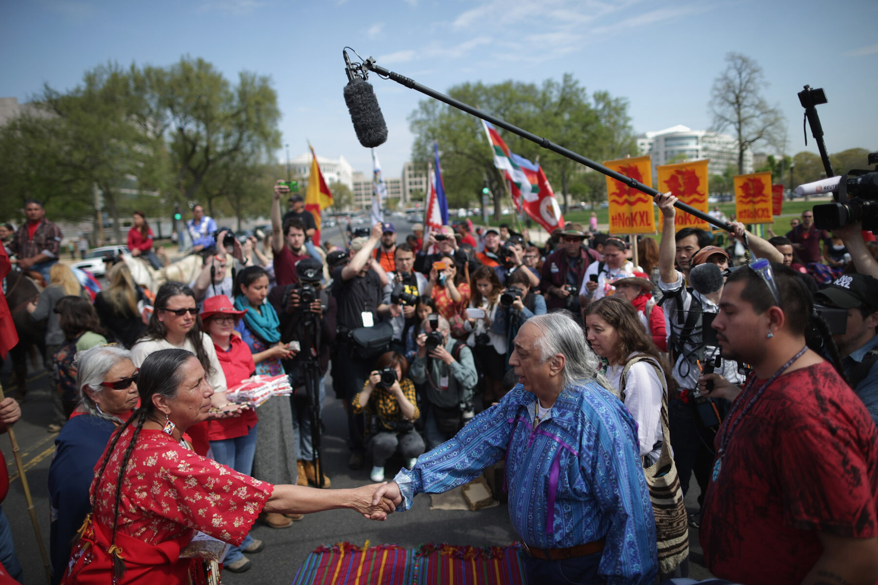 Photo of two people shaking hands surround by press and other people at a protest against a pipeline project.