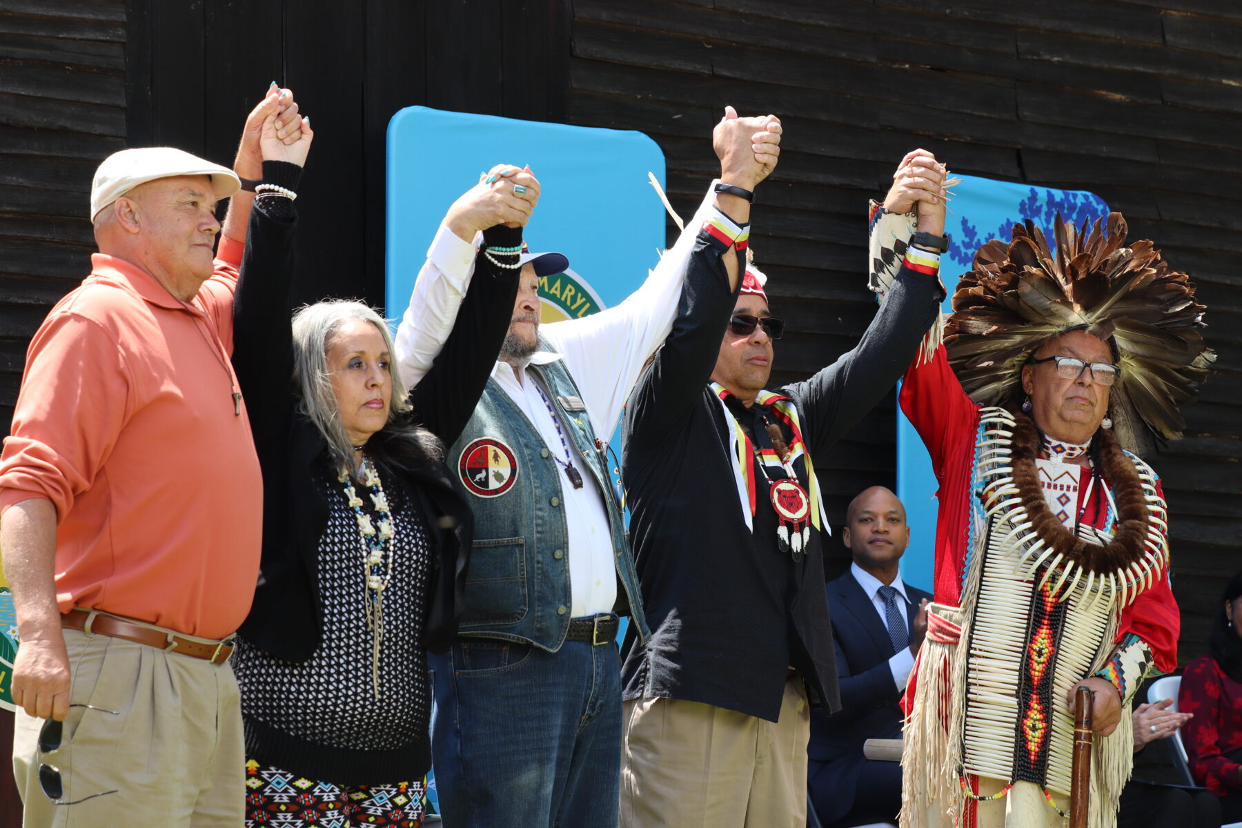 A color photo of five Indigenous people holding hands with their arms raised.