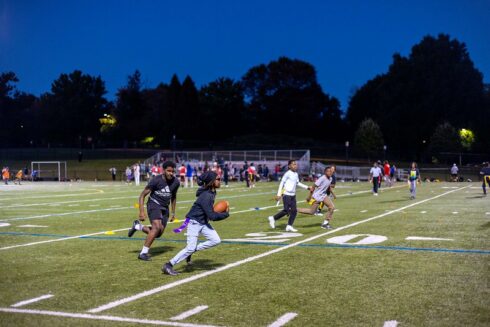 kids playing football on a field in the evening.