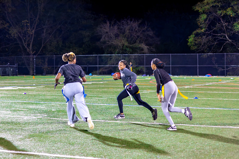 A group plays flag football on a lit athletic field